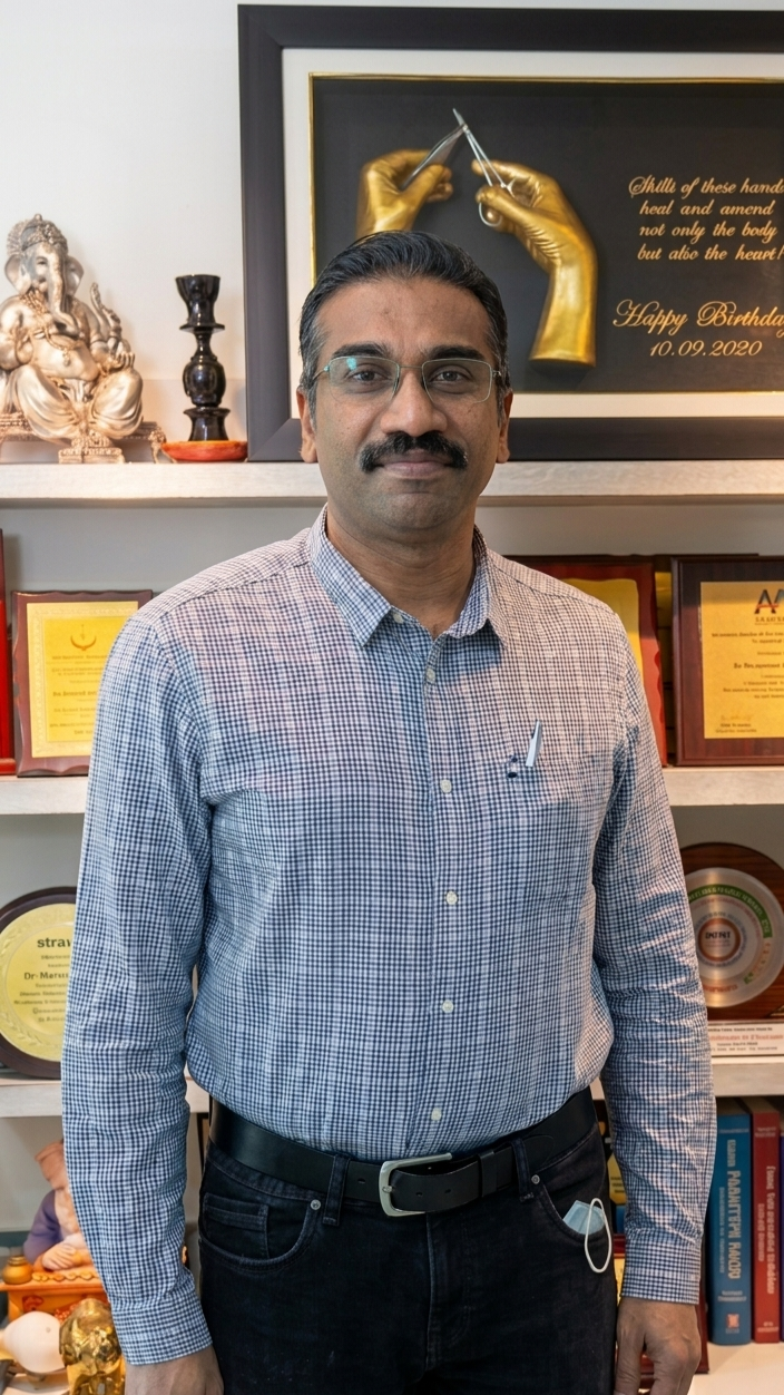 Dr. Santhosh Kumar Ravindran standing in his office in front of a bookshelf